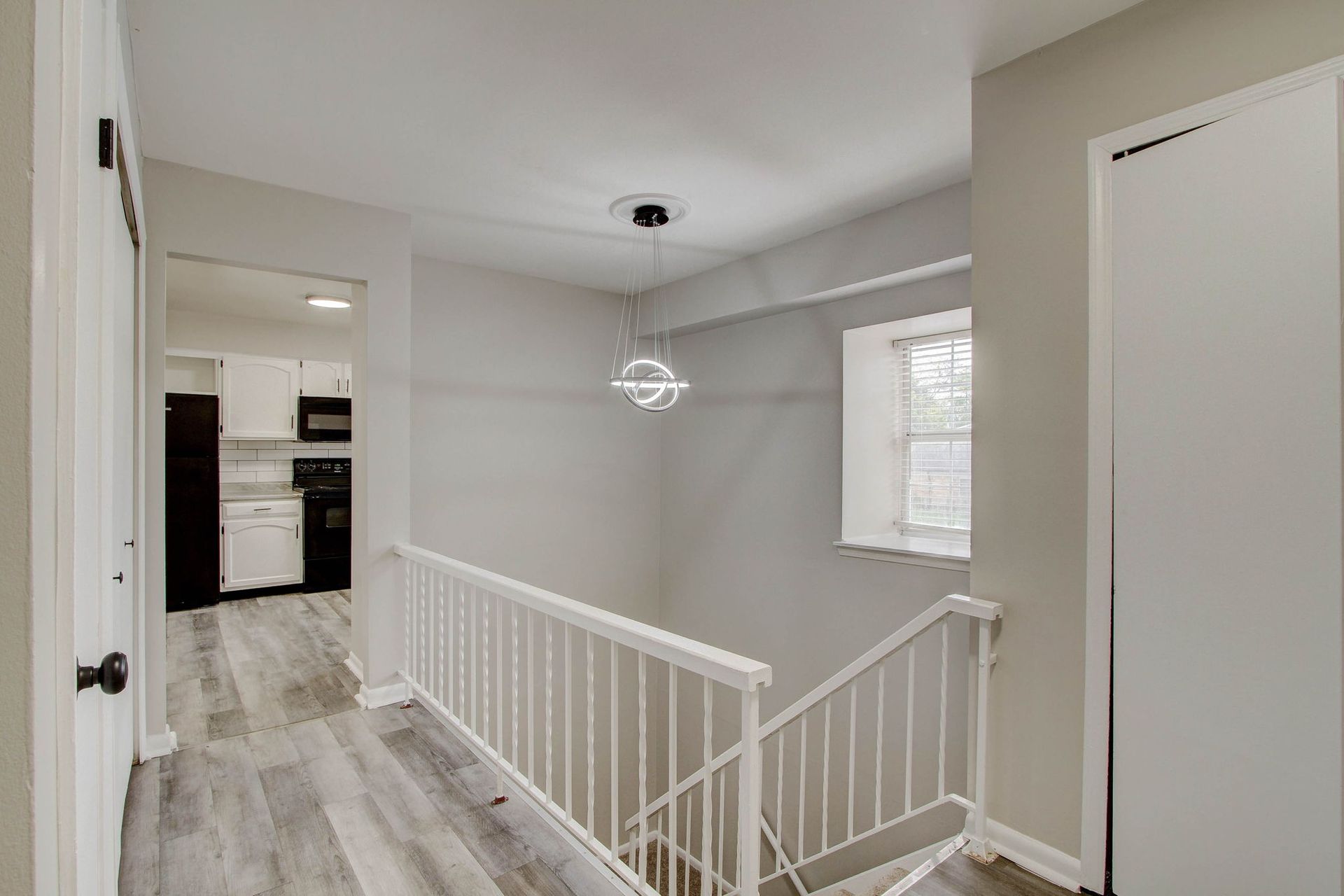 Hallway with stairs, white railing, window, and kitchen view. Gray walls and flooring.