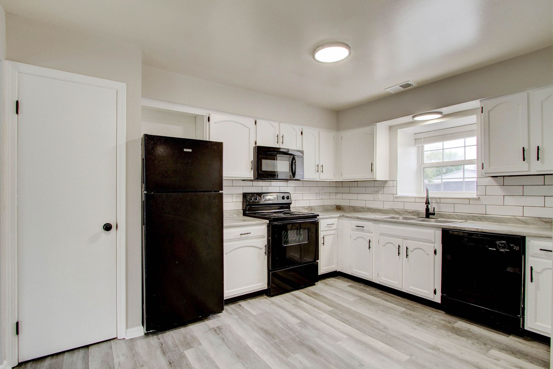 White kitchen with black appliances, light gray floors, and a window.