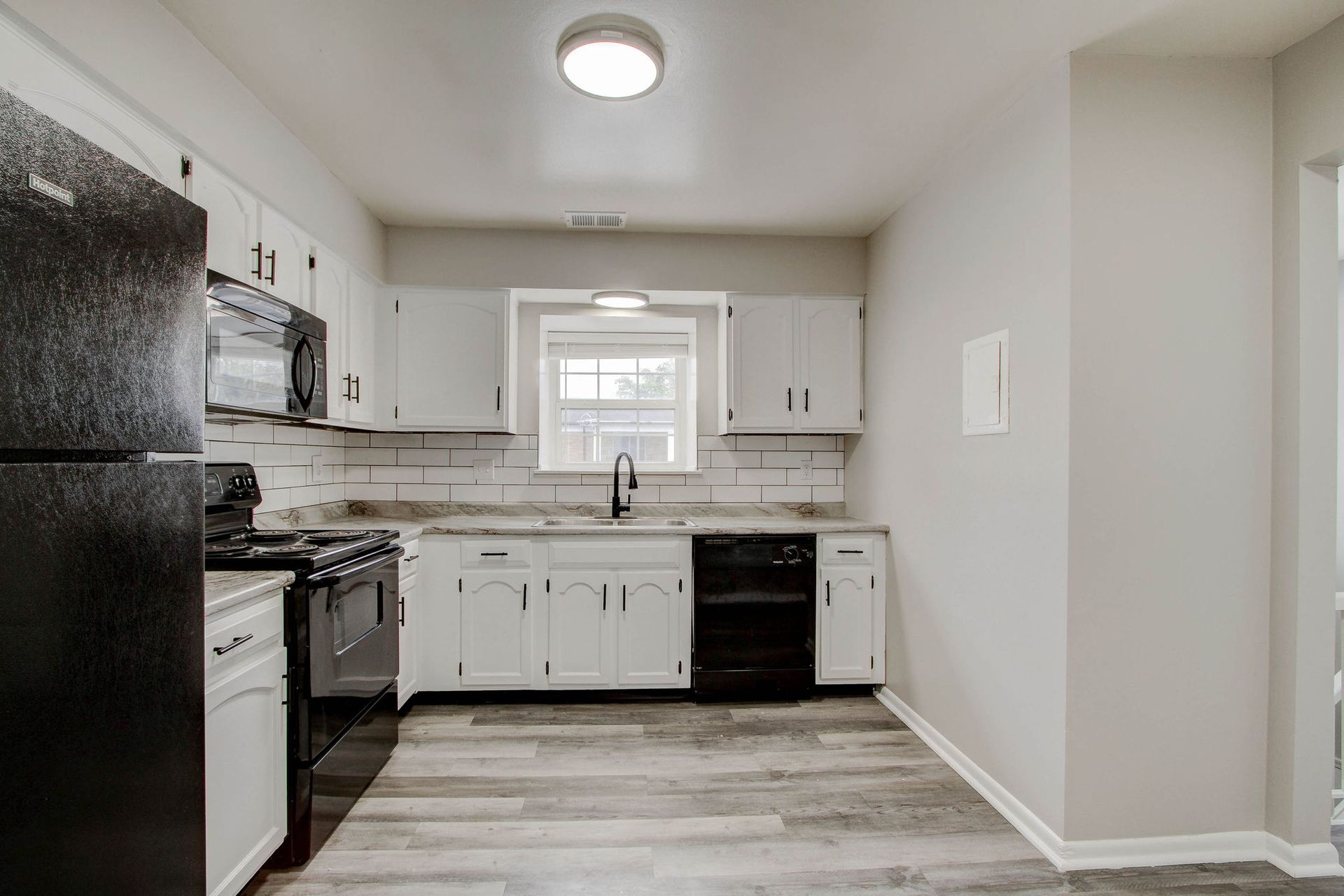 Kitchen with white cabinets, black appliances, and light gray flooring.