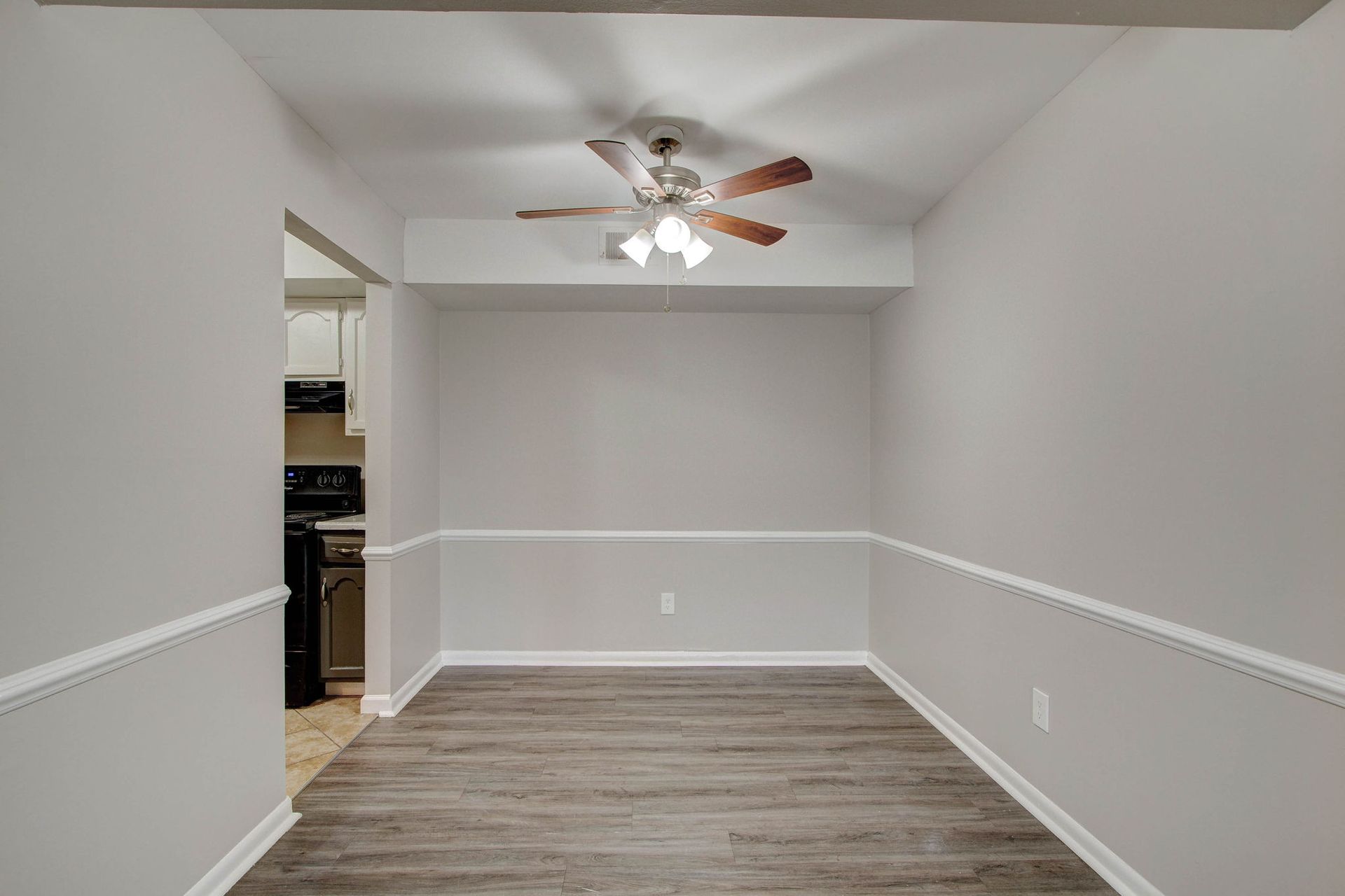 Dining room with gray walls, wood floor, white molding, and a ceiling fan.