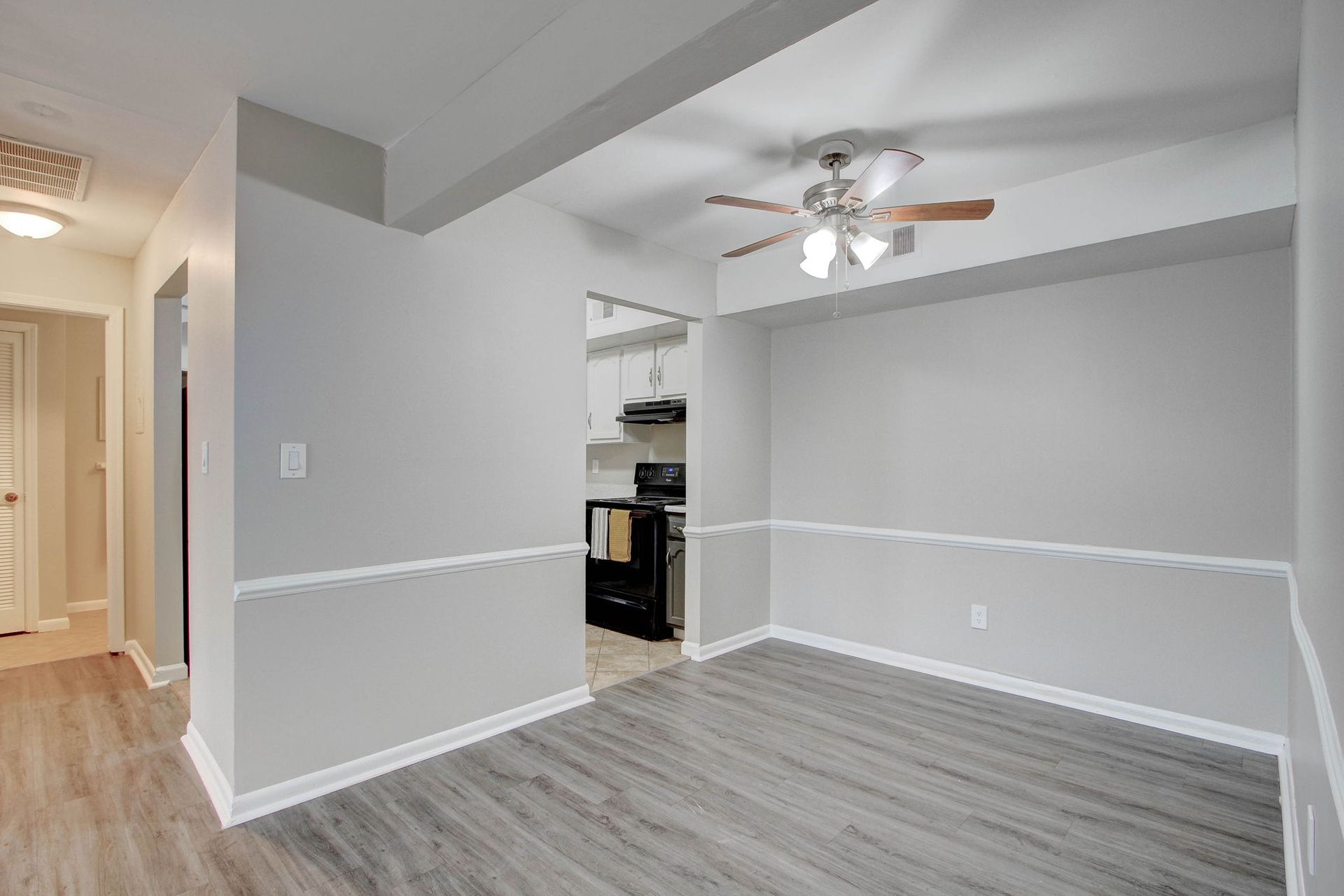 Dining room with gray walls, wood-look floors, doorway to kitchen; light fixture.