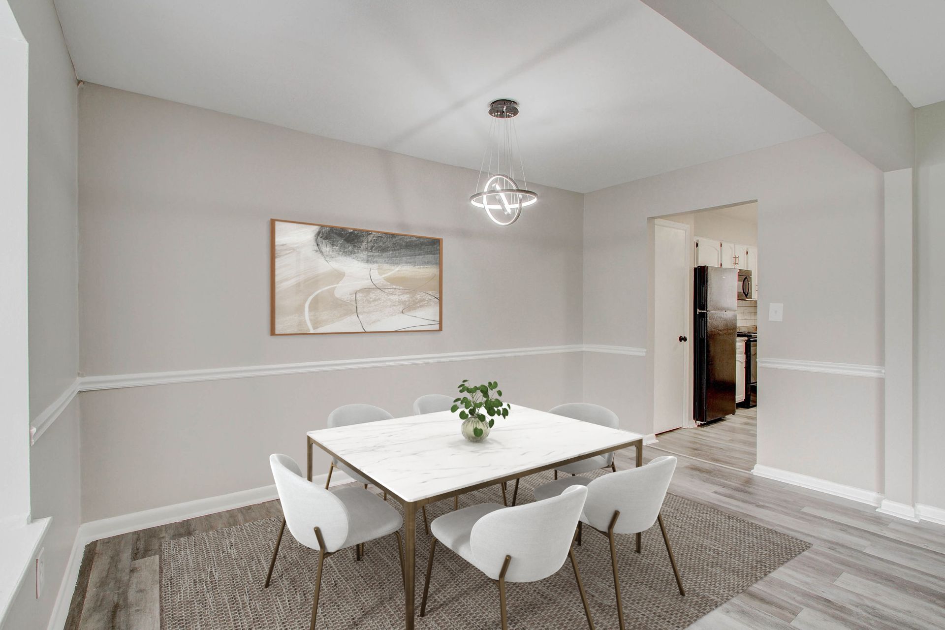 Dining room with table, chairs, artwork, and light fixture. Gray walls, wood floors, and view into a kitchen.