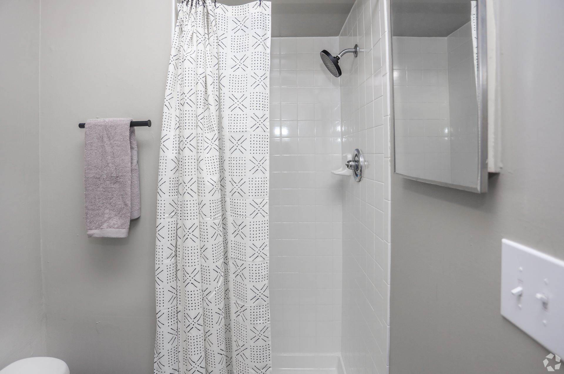 Bathroom with a white shower, light gray walls, towel rack with towels, and a medicine cabinet.
