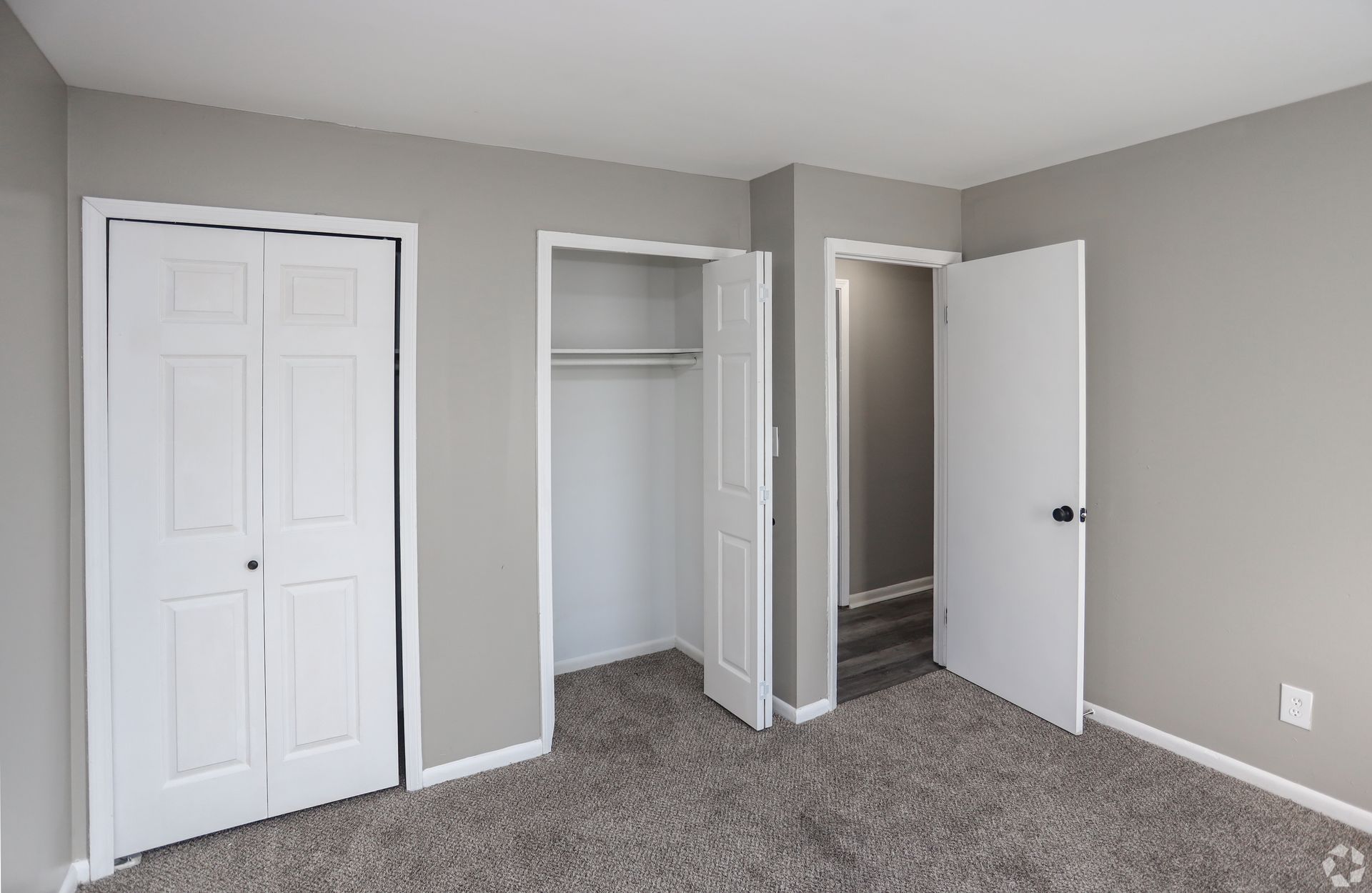 Bedroom with two closets, a doorway, and gray walls and carpet.