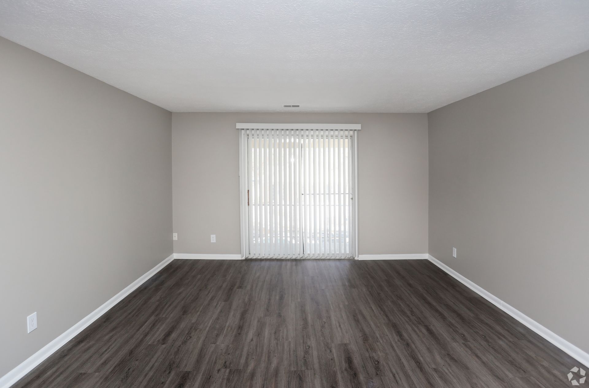 Empty room with gray walls, dark wood-look flooring, and sliding glass door covered by white vertical blinds.