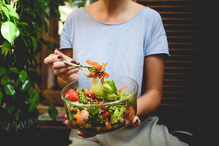 A woman is eating a salad from a bowl with a fork. A woman is eating a salad from a bowl with a fork.