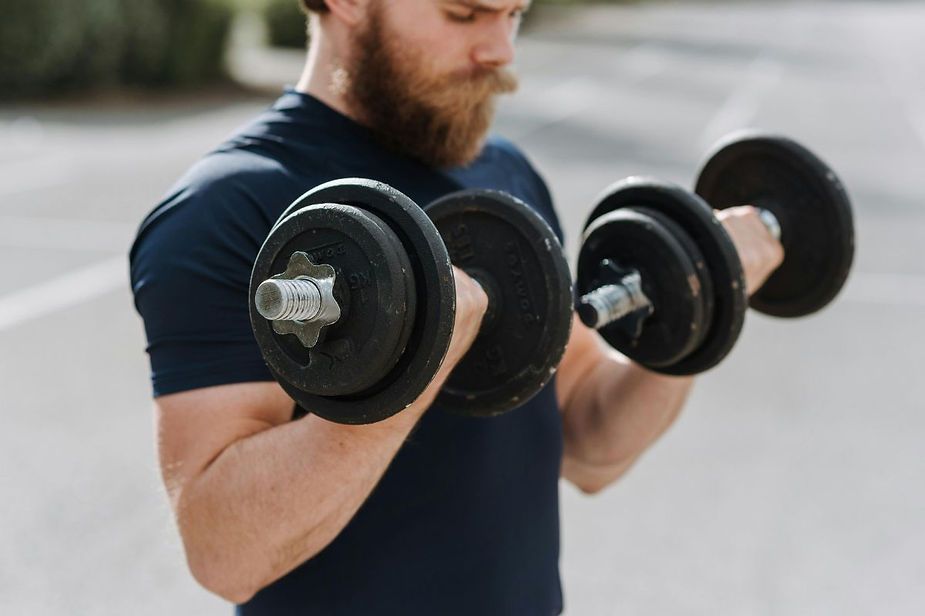A bearded man is lifting two dumbbells on his biceps. A bearded man is lifting two dumbbells on his biceps.
