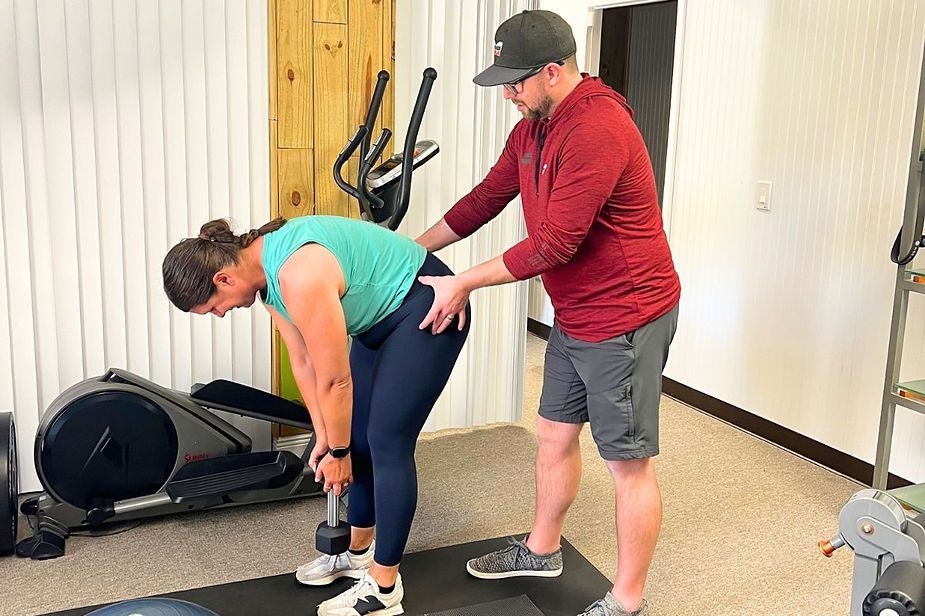 A man is helping a woman lift a dumbbell in a gym. A man is helping a woman lift a dumbbell in a gym.