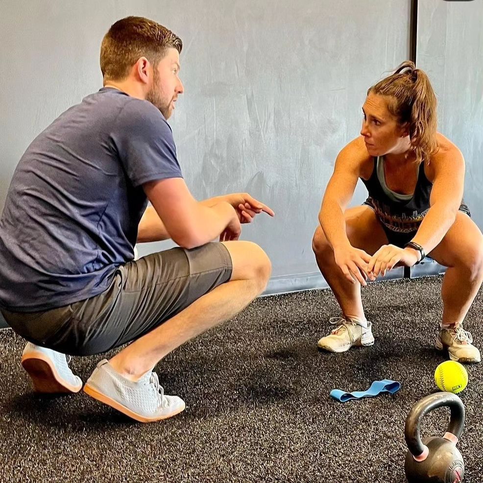 A man is helping a woman do exercises on a bench in a gym. A man is helping a woman do exercises on a bench in a gym.