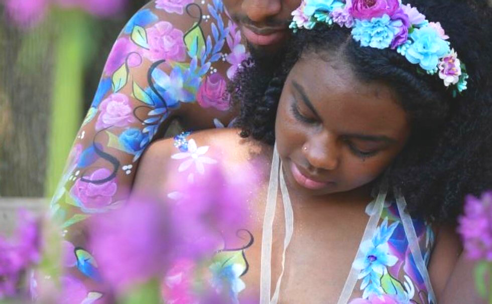 Two people in floral clothes and flower crowns posing in a soft-focus outdoor setting