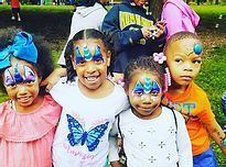 Five children with colorful face paint smiling outdoors in a park