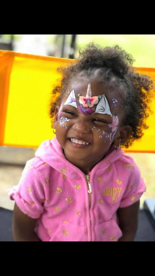 Smiling child with face paint and a pink hoodie, sitting in front of a yellow background