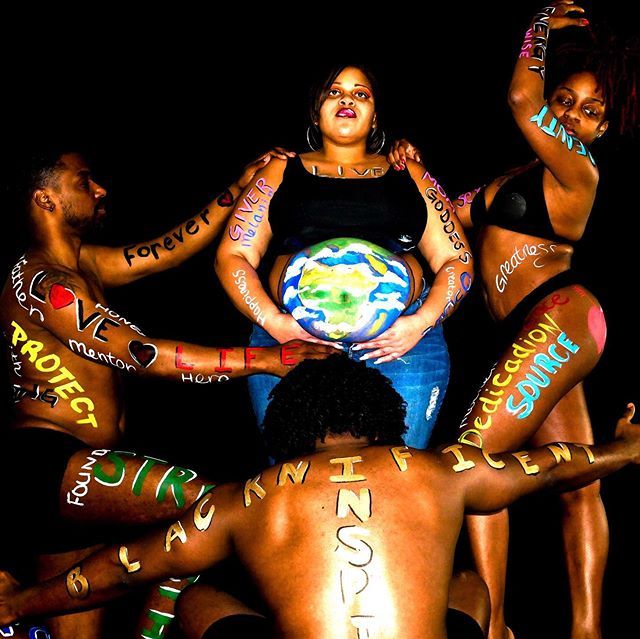 People posing with painted slogans around a central figure holding a painted Earth sphere on a black background