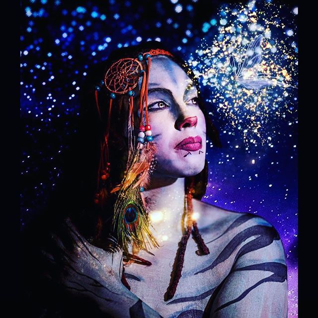 Woman with dreamcatcher hair art gazing upward against a starry blue-purple backdrop