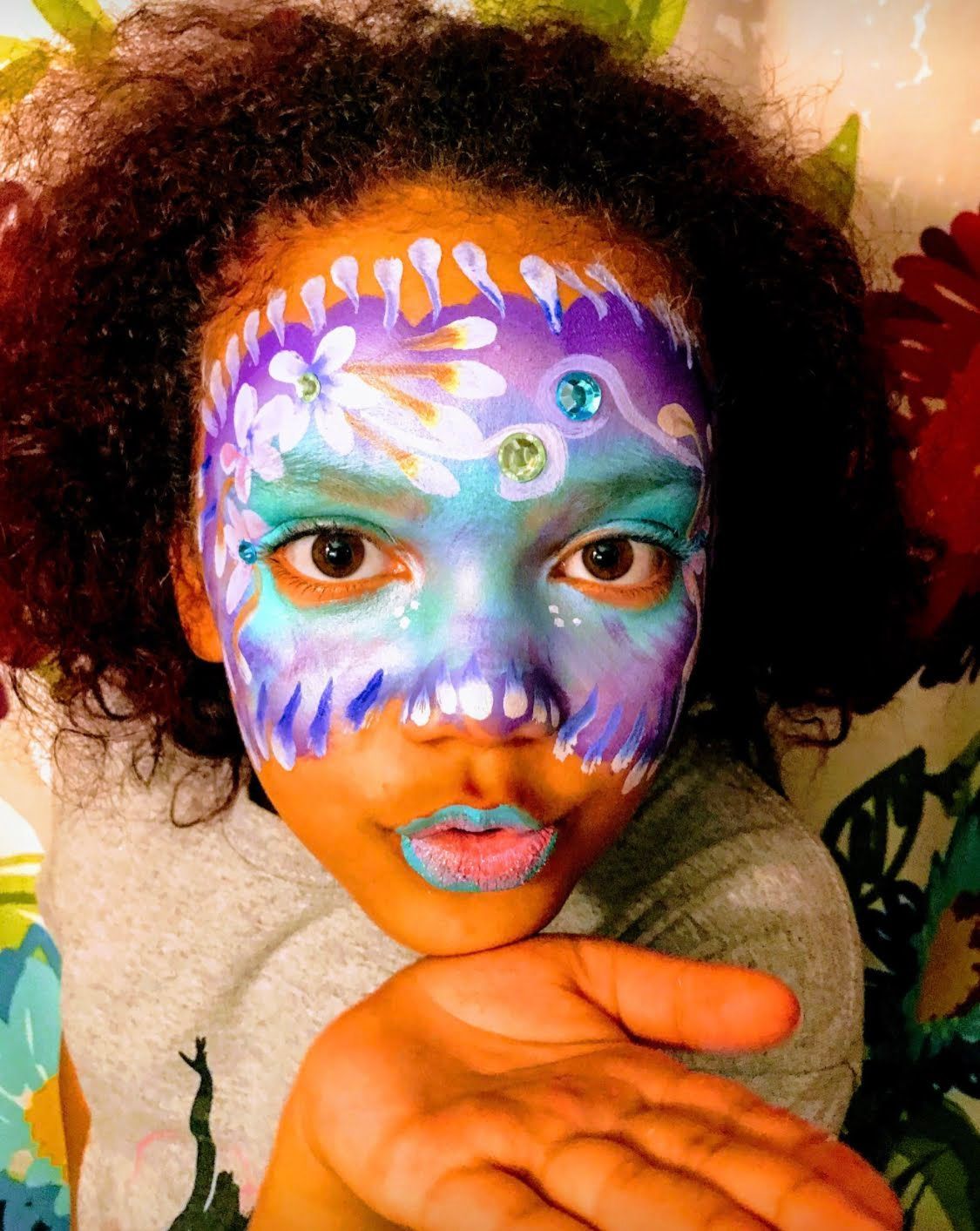 Little girl's face painted, blowing a magical kiss.