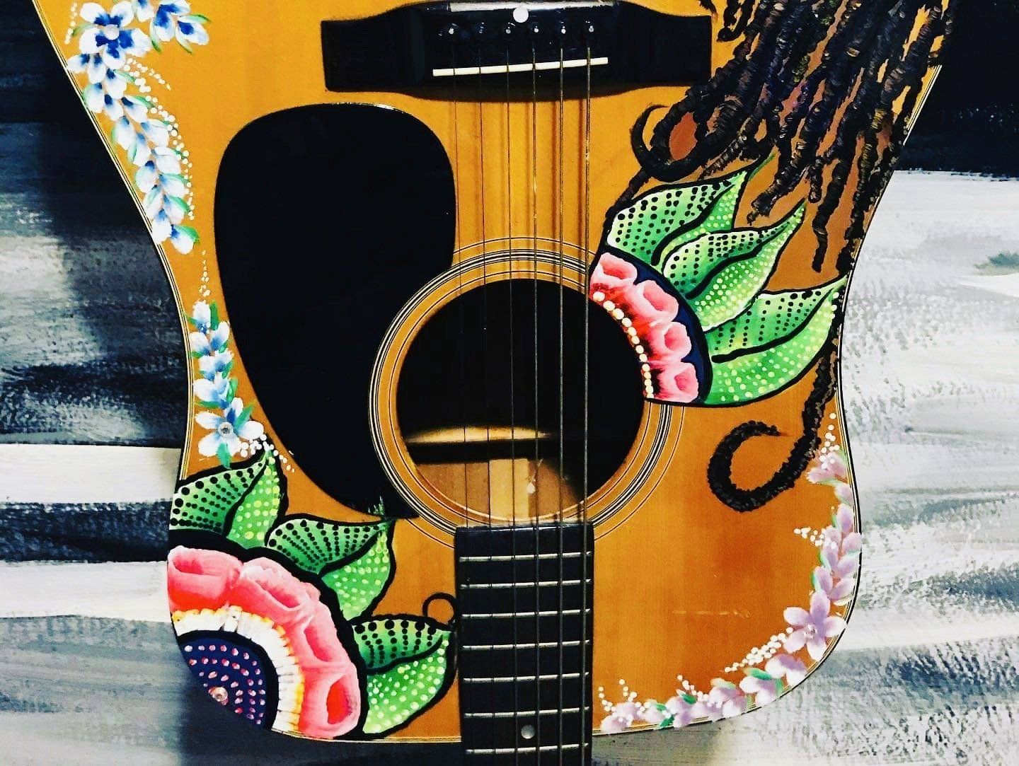 Colorfully painted acoustic guitar with floral and leaf designs on a yellow body and black neck