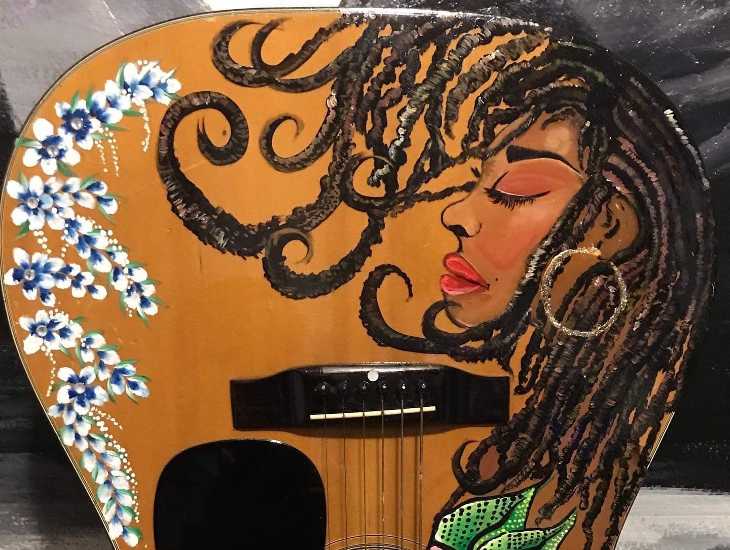 Decorated guitar with a painted woman’s face, flowing hair, and white flowers on an orange background