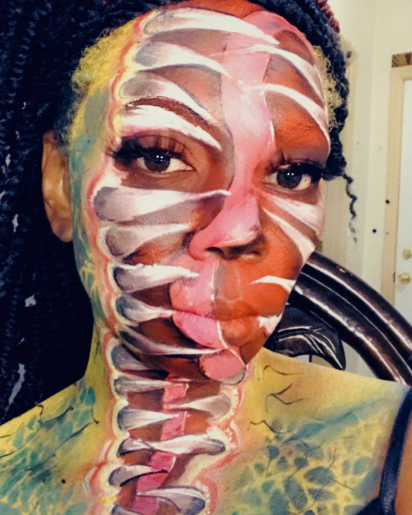 Close-up portrait with white and red face paint on a person, indoors, against a chair back