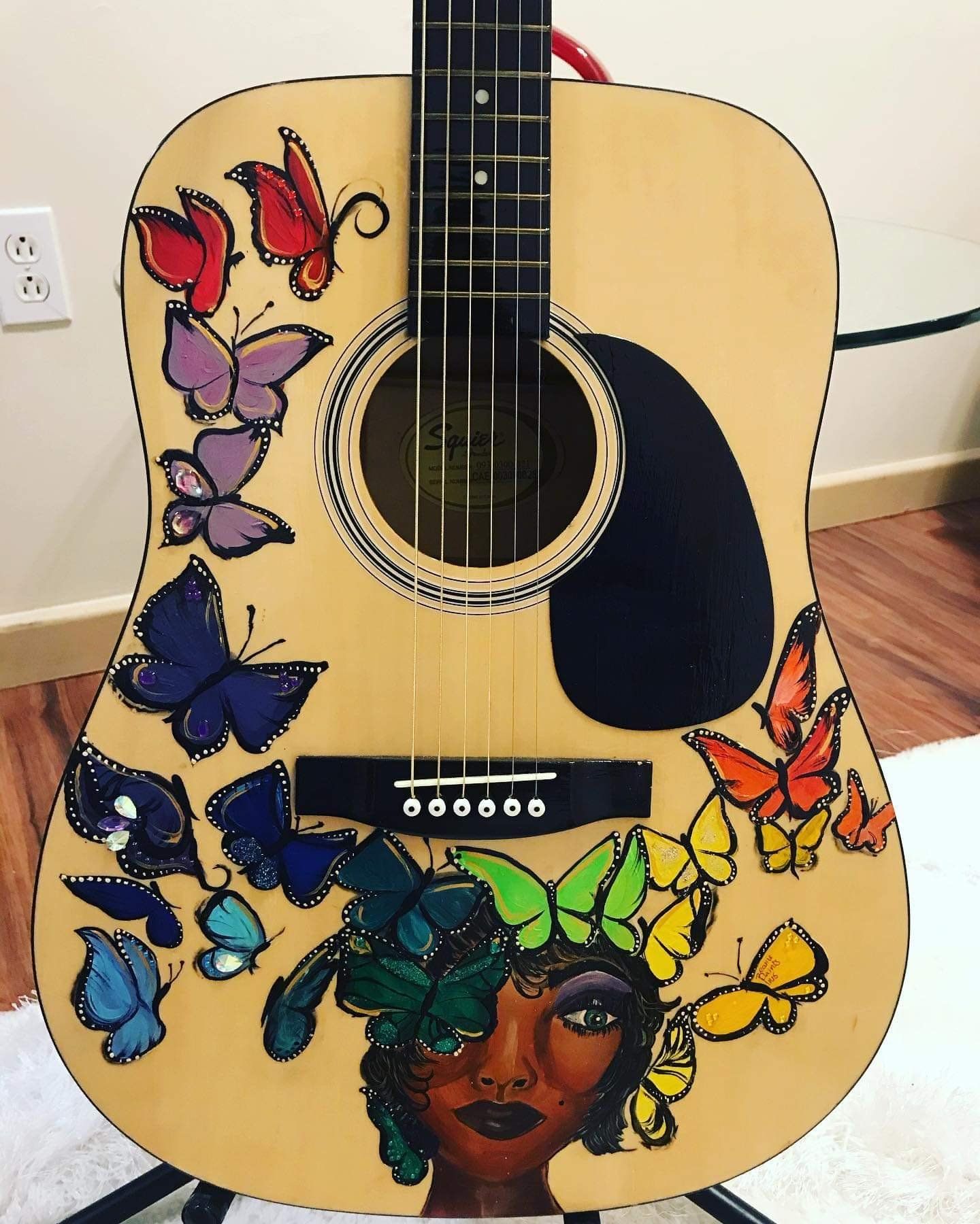 Acoustic guitar with colorful butterfly and woman-face artwork on a light wood body