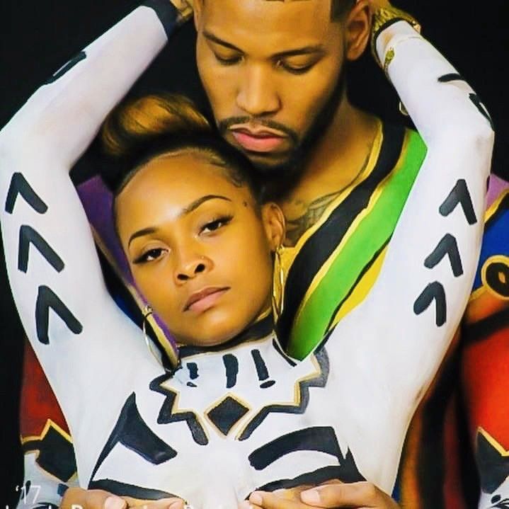 Two people posing closely together in bold patterned outfits, one resting their head on the other's chest.