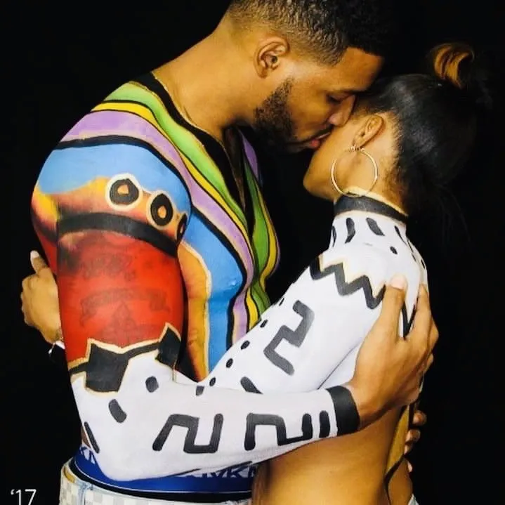 Two people embracing and kissing, wearing colorful patterned sweaters on a dark background.