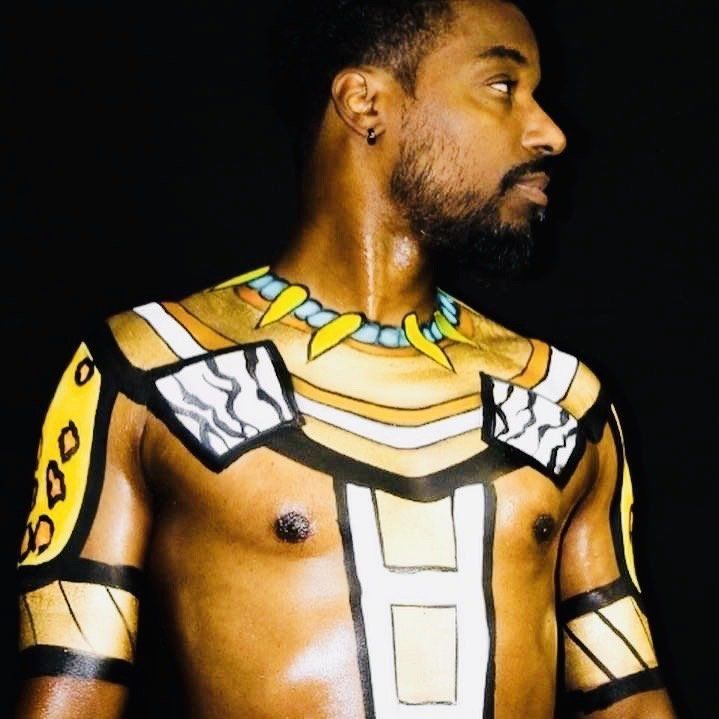 Man with black-and-gold body paint, shown in side profile against a dark background