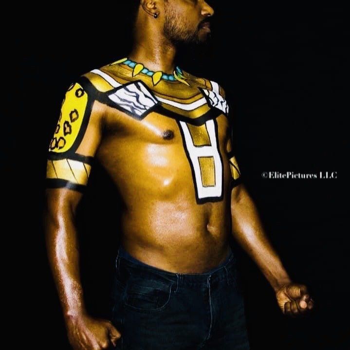 Person posing shirtless with geometric yellow and white body paint on a dark background