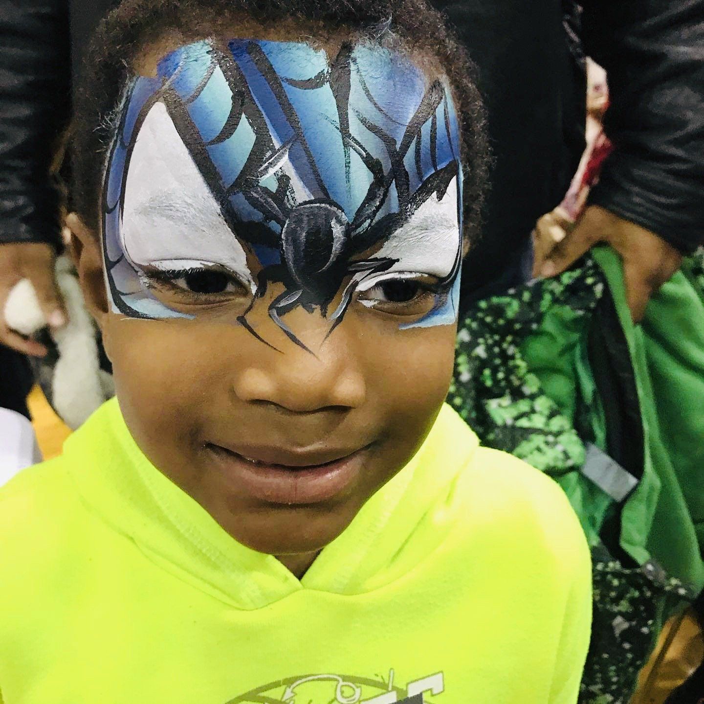 Child with blue-and-black face paint and a neon yellow shirt smiling at a costume event