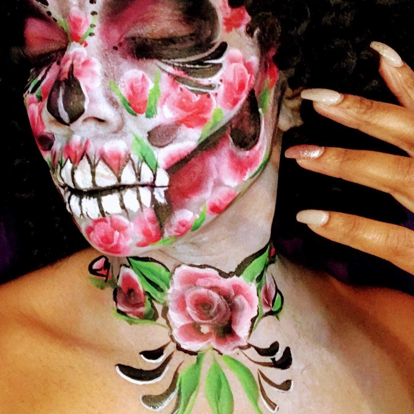 Person with pink floral skull face paint and matching neck tattoo, hand raised beside face