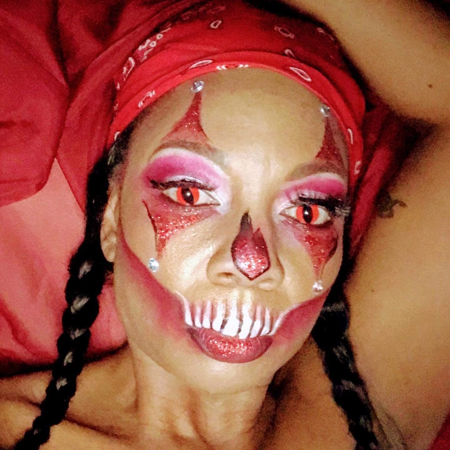Person with skull-inspired face paint, red bandana, and braided hair lying on a red pillow