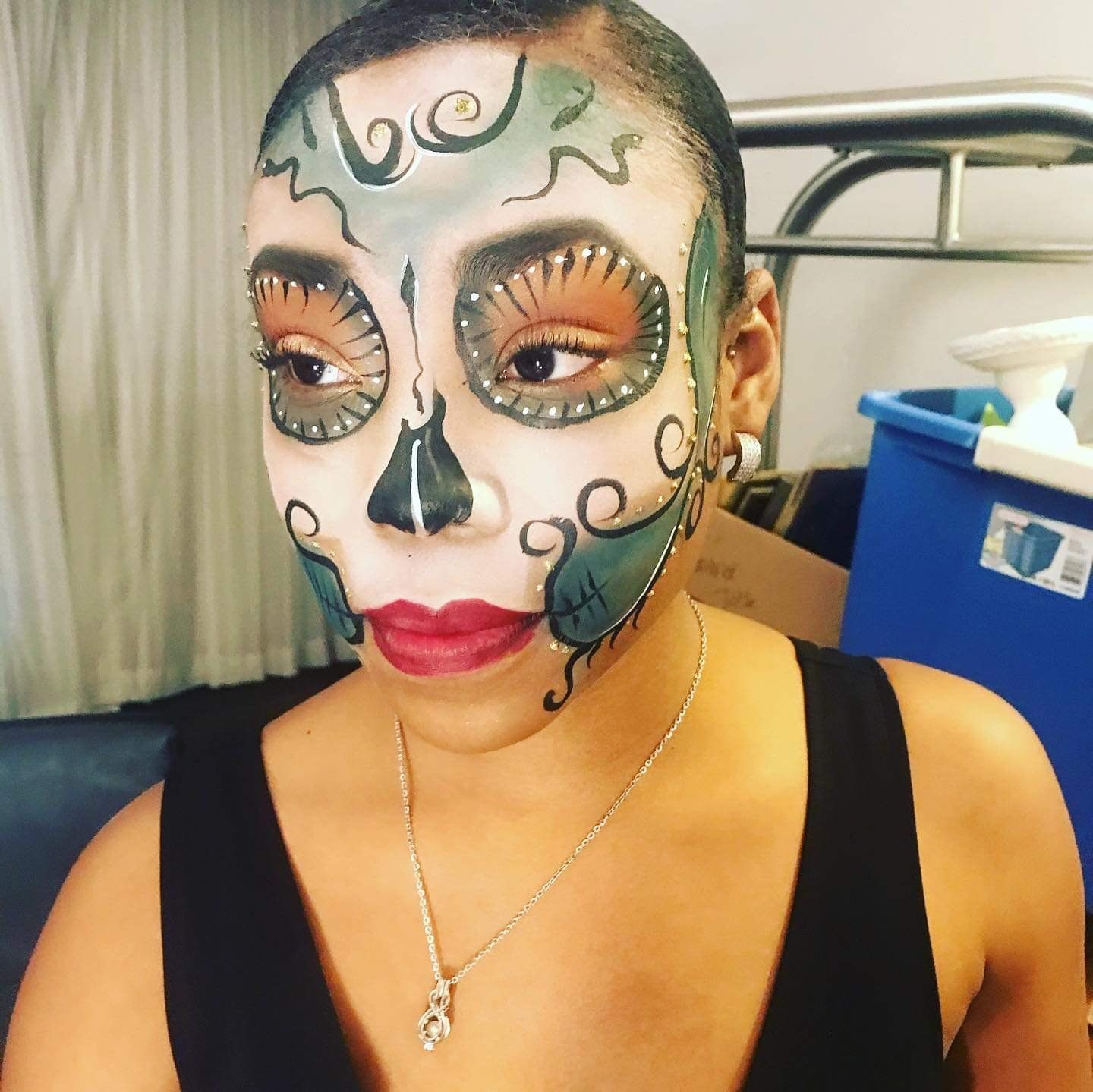 Person with Day of the Dead face paint, black top, and necklace, standing indoors.