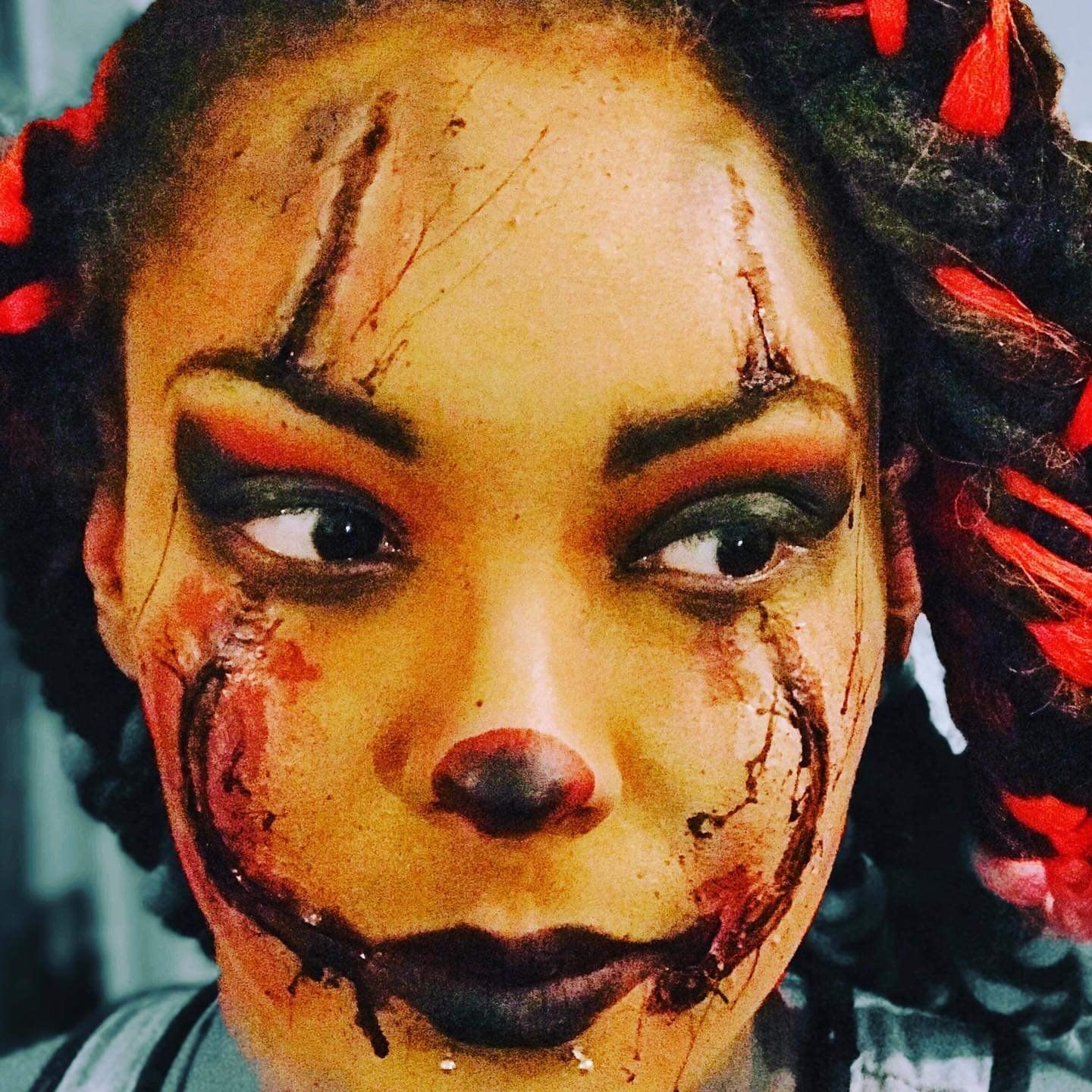 Close-up of a person in spooky clown makeup with red streaks and dark lipstick, looking to the side.