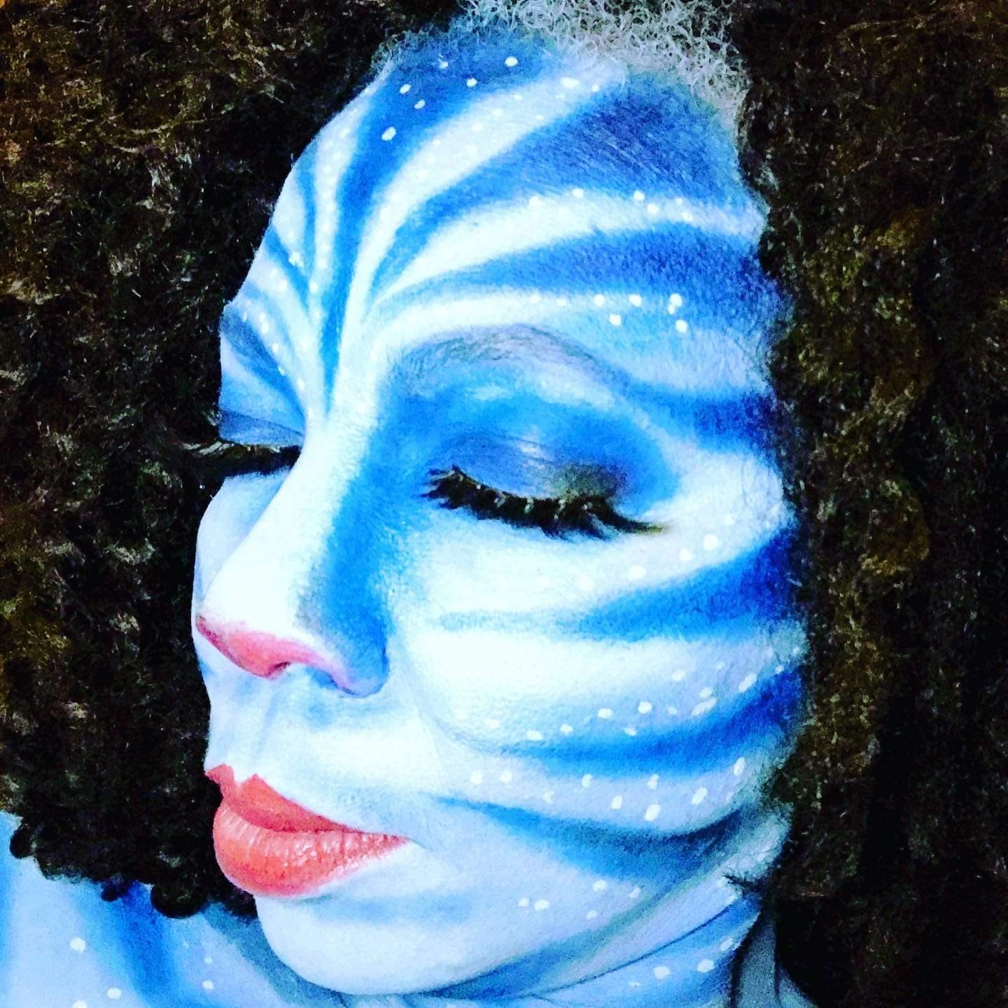 Blue-and-white face paint on a close-up portrait with closed eyes and curly dark hair