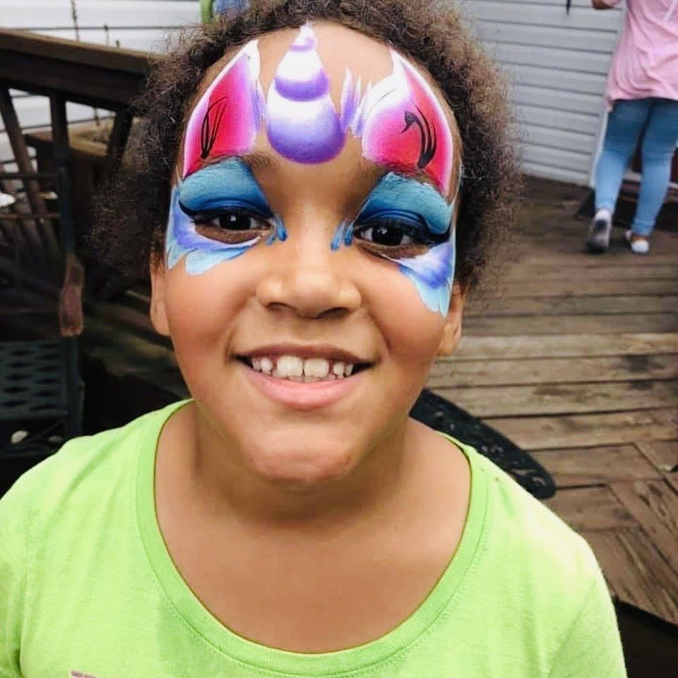 Smiling child with colorful unicorn face paint standing on a wooden deck