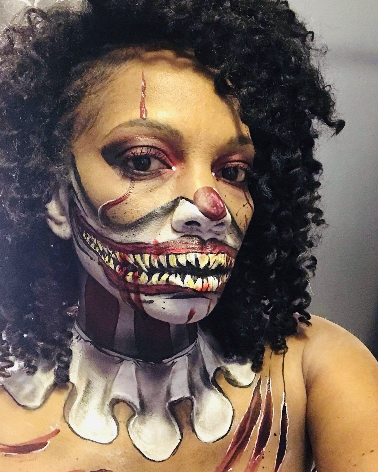 Person in clown-inspired face paint and curly wig, with a painted skull collar and eerie teeth design.
