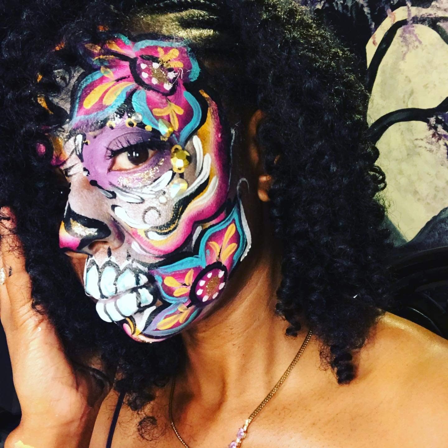 Close-up of a face with vibrant rainbow skull makeup and curly black hair