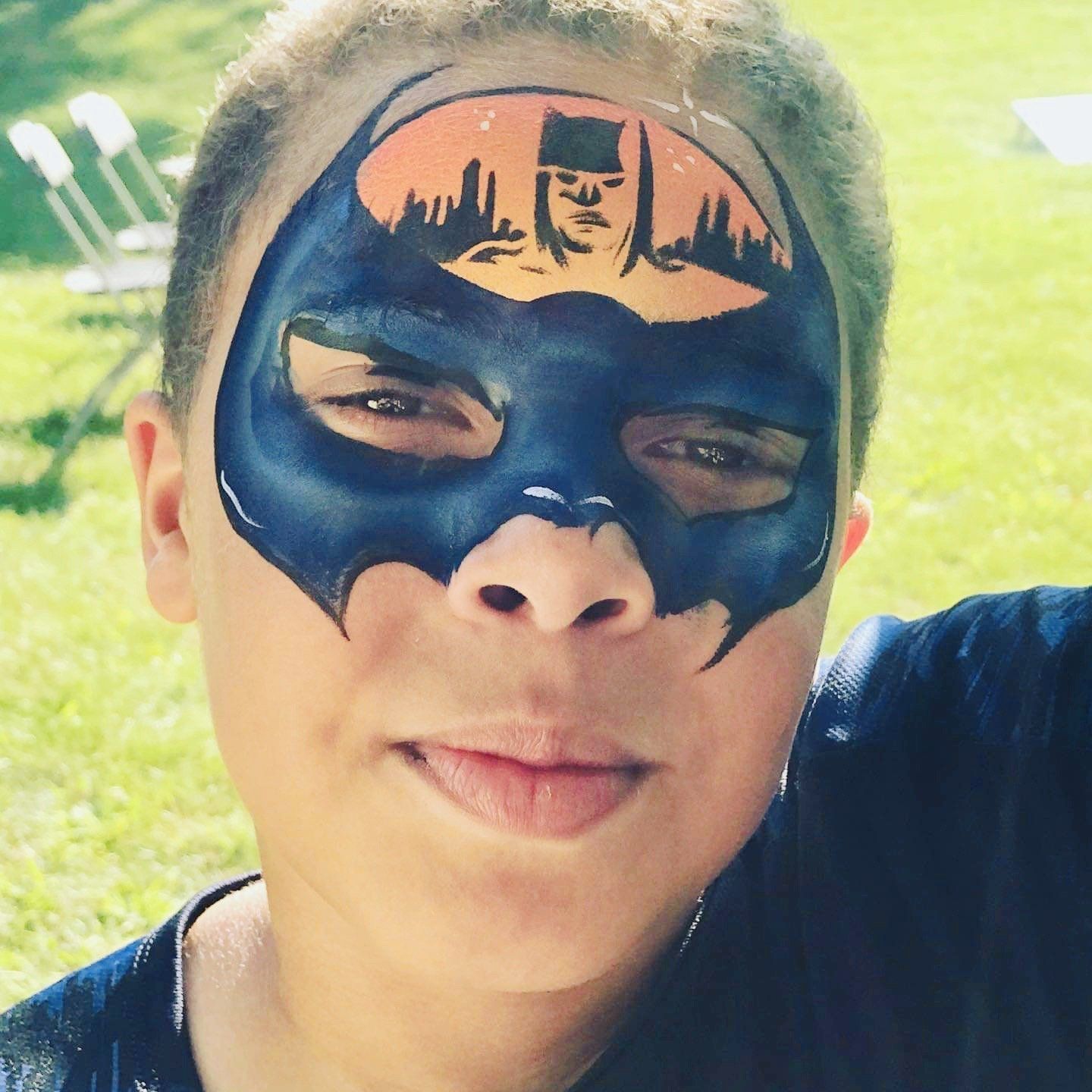 Close-up of a person wearing a black Batman-style mask outdoors in bright sunlight