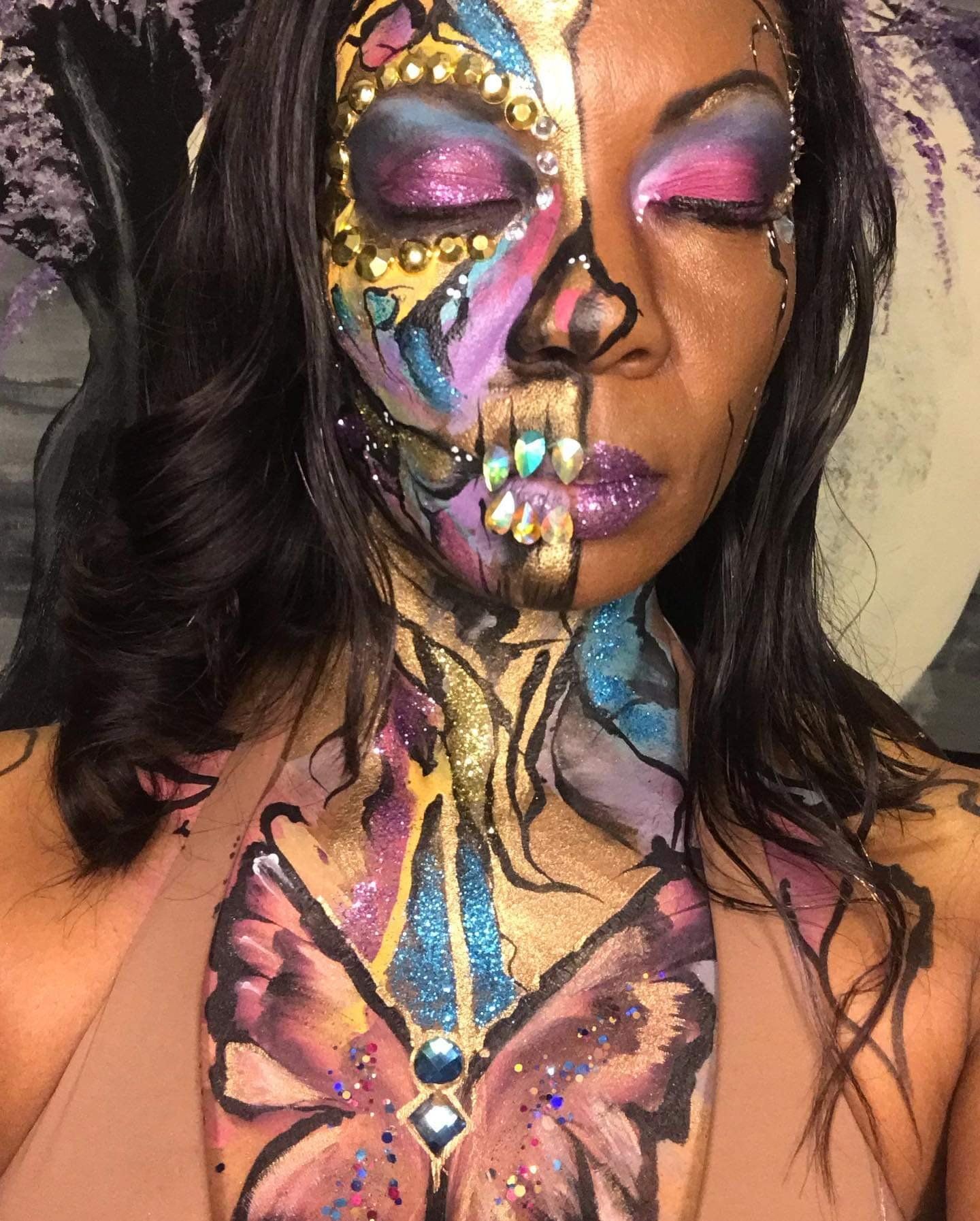 Close-up of a face and chest painted with colorful butterfly and abstract body art.