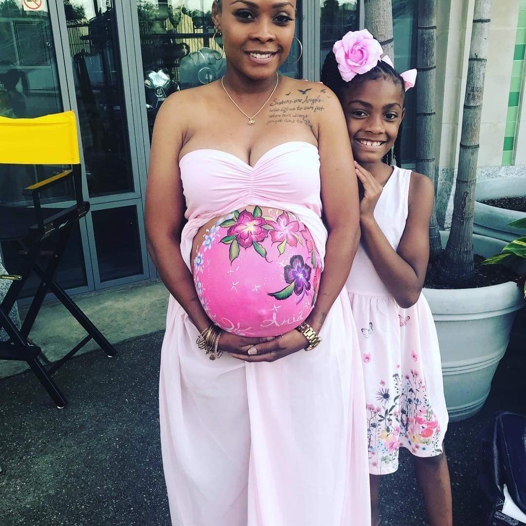 Pregnant woman and girl in pink dresses standing outside, holding a decorated pink balloon