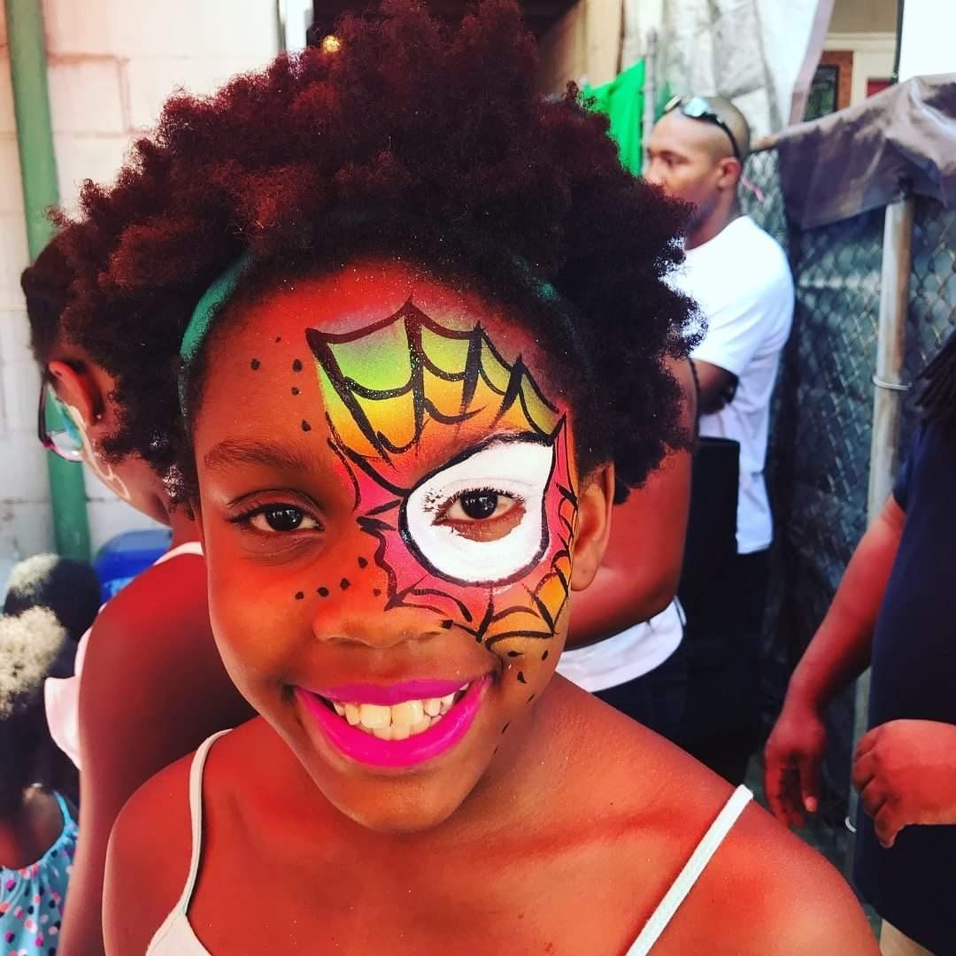 Smiling child with red-and-yellow face paint in a festive outdoor setting