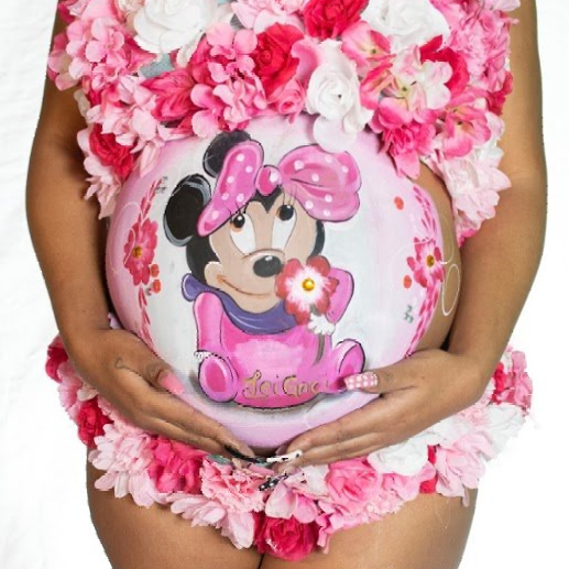 Pregnant belly painted with Minnie Mouse and pink flowers, framed by a pink floral dress.