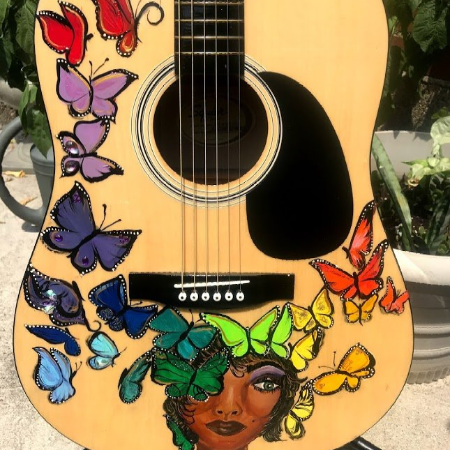 Acoustic guitar decorated with colorful butterflies and a painted face on the body