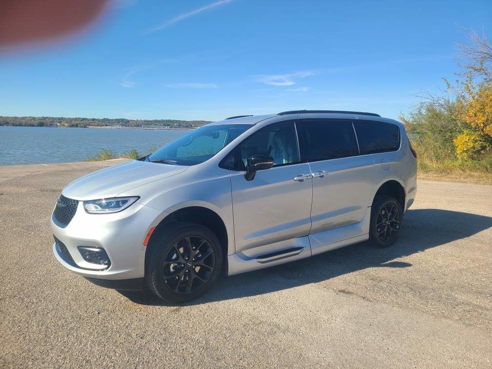 Silver minivan parked by a lakeside road under a clear blue sky