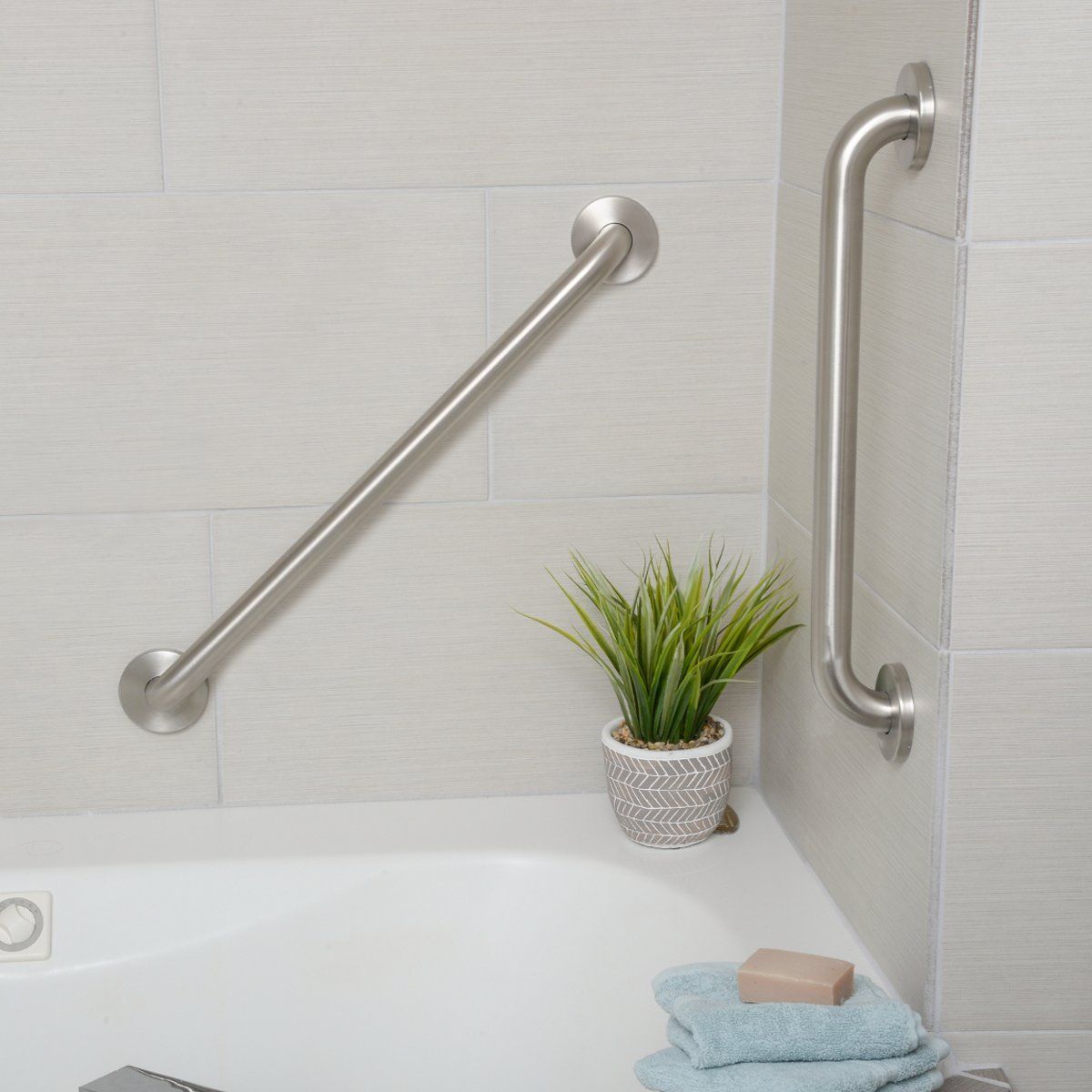 Modern bathtub with stainless grab bars, potted plant, soap, and folded towels in a bright bathroom