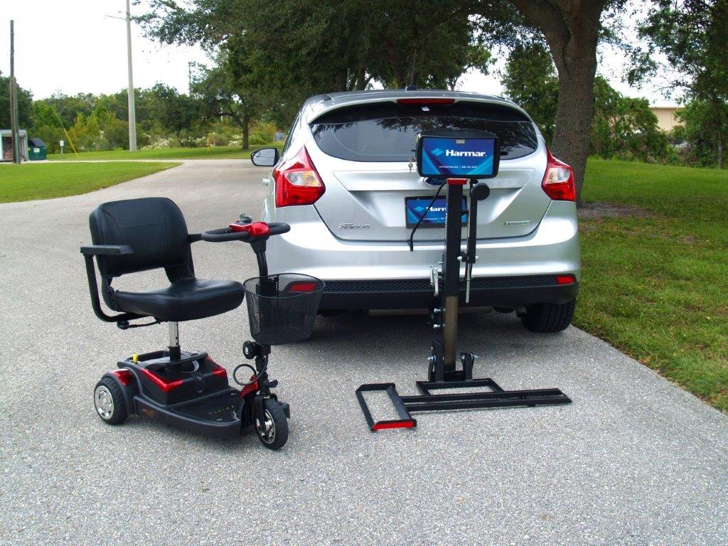 White SUV on a road with two mobility scooters behind it, one black and one mounted to a lift rack.