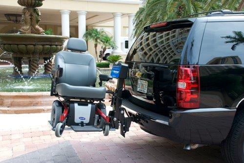Motorized wheelchair attached to the rear of a black SUV in a hotel driveway