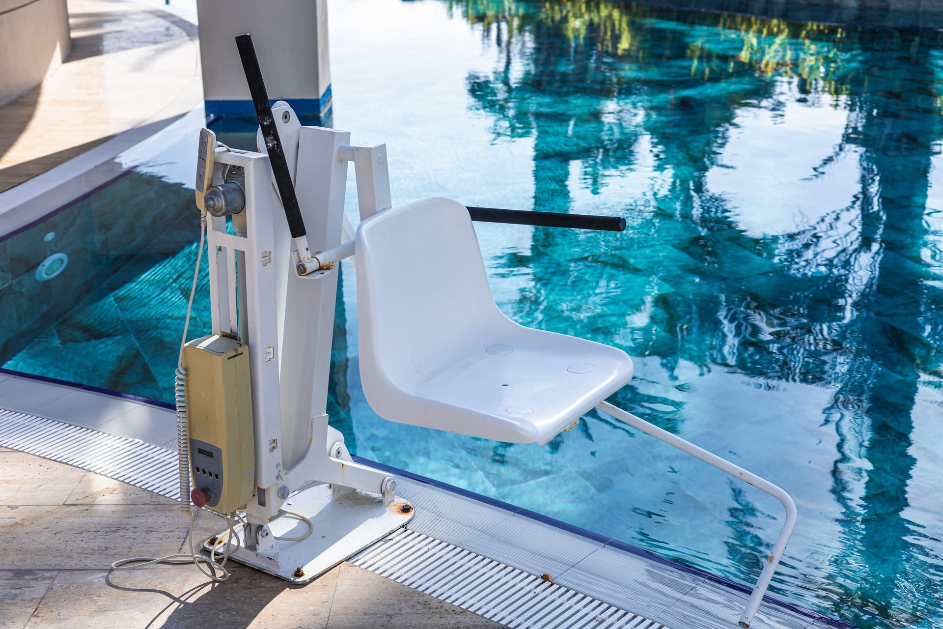 Poolside wheelchair lift beside a blue swimming pool with a white seat and metal railings