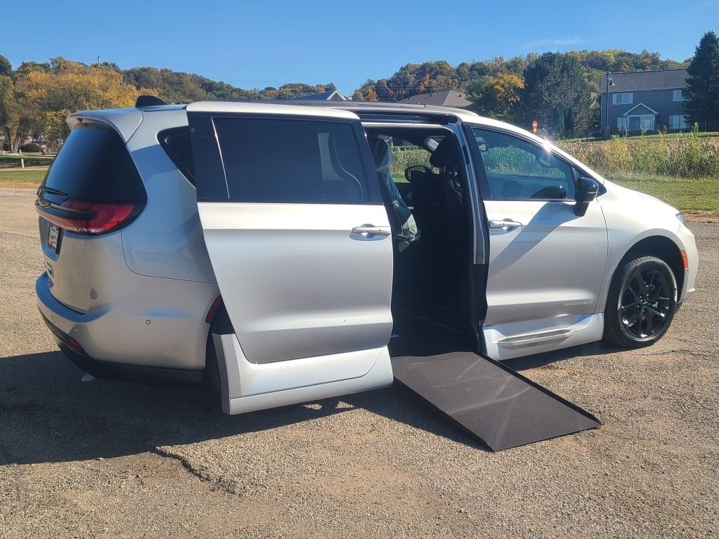 Silver minivan with sliding door open and wheelchair ramp extended on a sunny outdoor lot