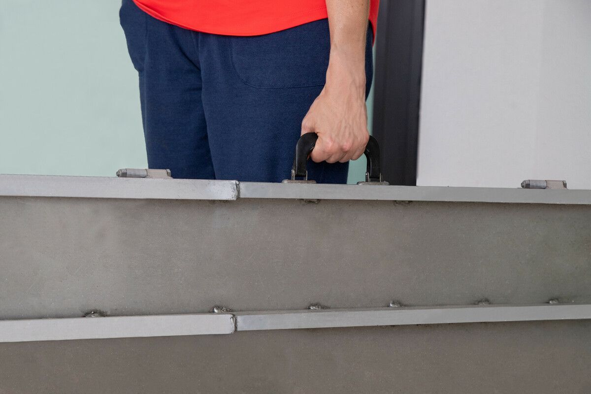 Person in a red shirt holding a black handle behind a gray barrier.