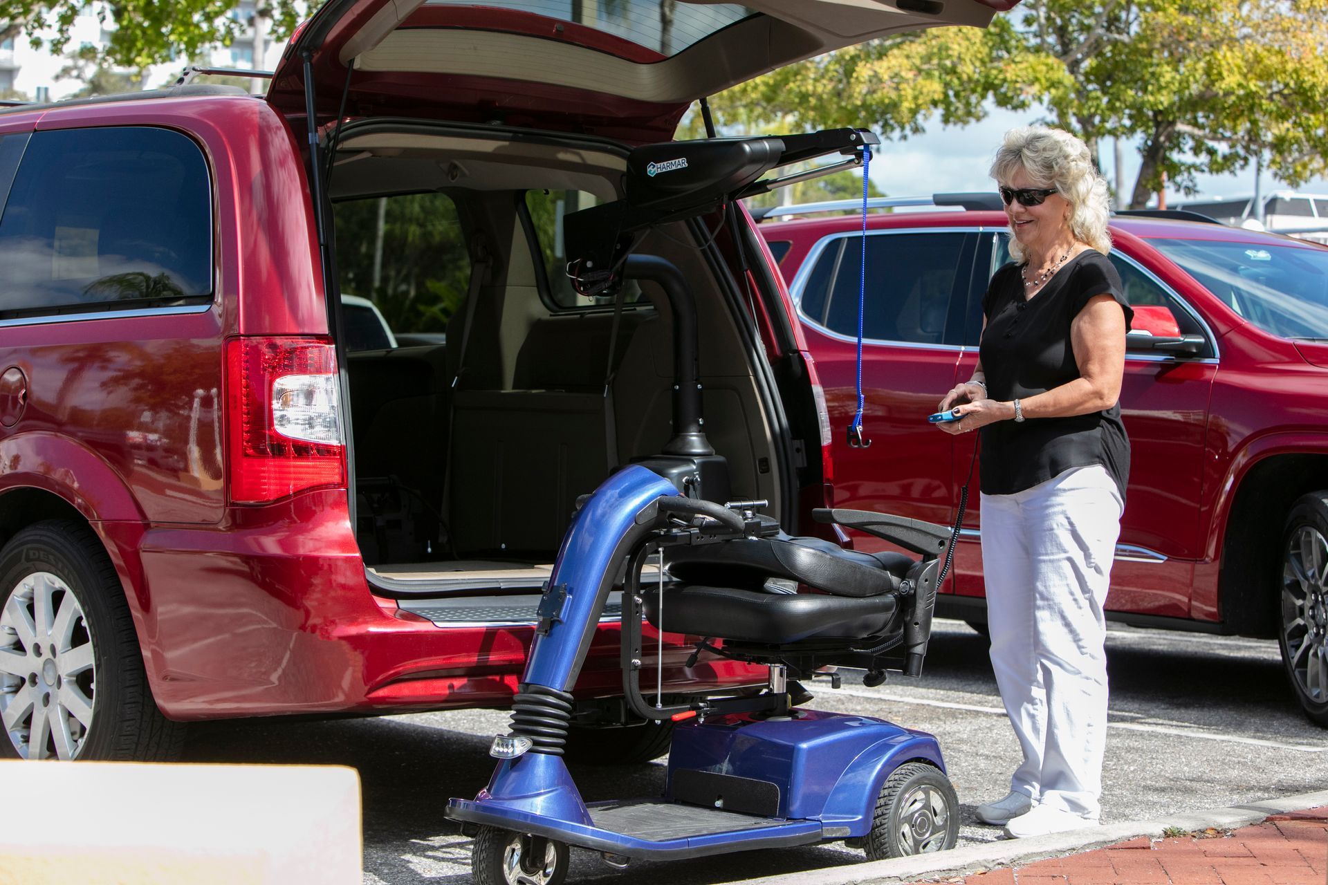 Woman using a blue vacuum to clean the open trunk of a red SUV in a parking lot